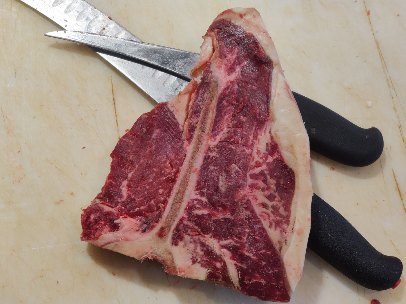 Raw T-bone steak on a cutting board beside butcher knives