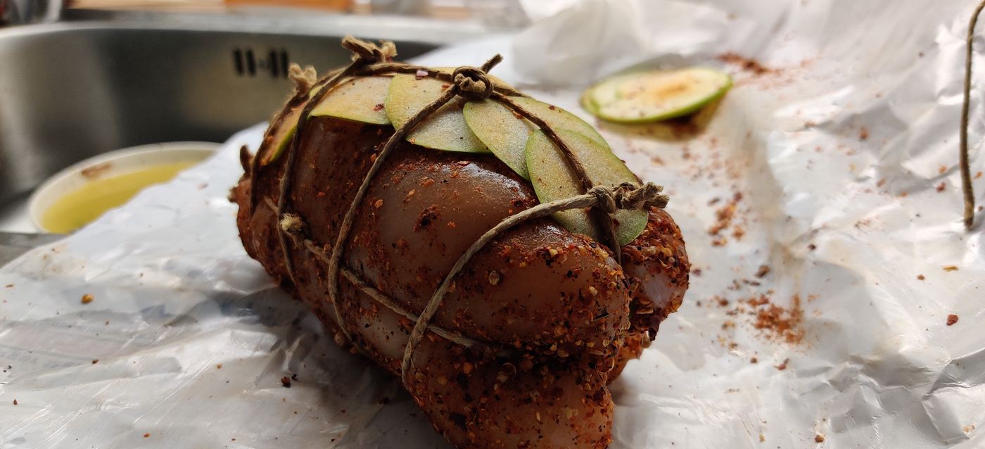 A seasoned, trussed roast topped with sliced apple, ready for the grill