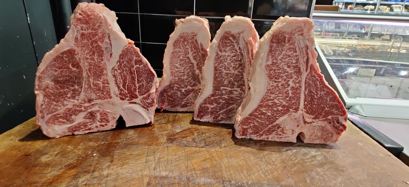 Four dry-aged, heavily marbled steaks lined up at the butcher counter