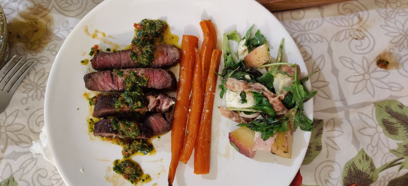 Full plated dinner with sliced steak, glazed carrots, and a fresh salad